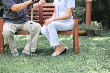 Hemşire ile hasta birlikte konuşurken bankta oturan. Asyalı yaşlı adam ve birlikte konuşurken oturan bir genç bayan. Ruh sakin ol.