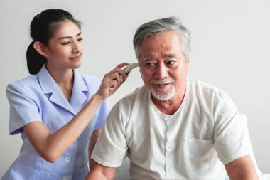 Güzel hemşire yaşlı adam yüksek teknoloji sıcaklık ölçüm aracını kullanarak. Yatakta çekici Asyalı kadın hemşire ile beyaz sakallı üst düzey Asya adam. Üst düzey emeklilik ev Servisi, bakım alıcı kavramı.