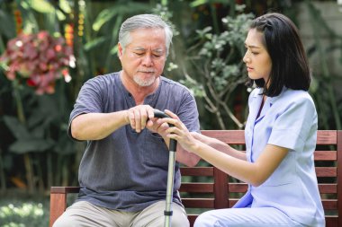 Hemşire ile hasta birlikte konuşurken bankta oturan. Asyalı yaşlı adam ve birlikte konuşurken oturan bir genç bayan. Ciddi ruh hali.