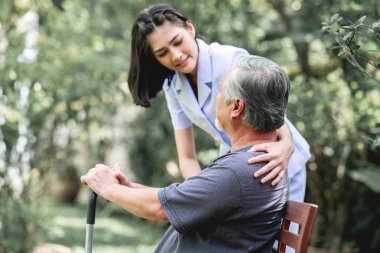 Hemşire ile hasta birlikte konuşurken bankta oturan. Asyalı yaşlı adam ve birlikte konuşurken oturan bir genç bayan. Ruh sakin ol.