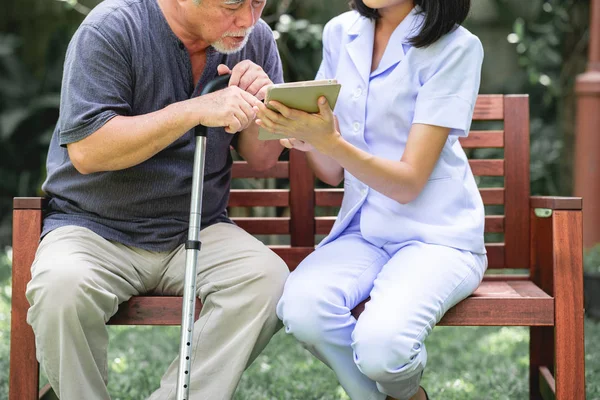 Hemşire hasta birlikte tablet vasıl seyir bankta oturmuş ile. Asyalı yaşlı adam ve birlikte konuşurken oturan bir genç bayan. Ruh sakin ol.