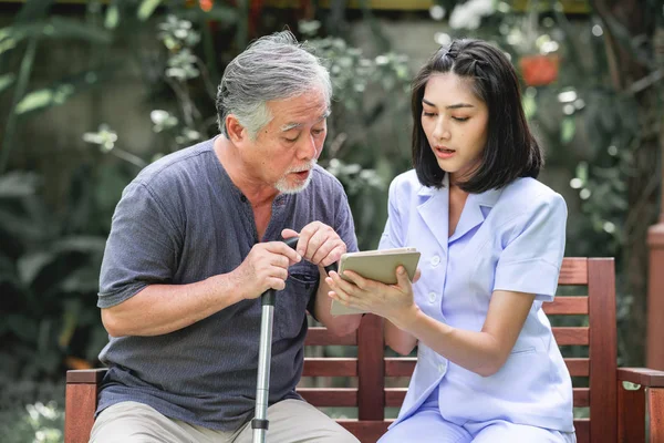 Hemşire hasta birlikte tablet vasıl seyir bankta oturmuş ile. Asyalı yaşlı adam ve birlikte konuşurken oturan bir genç bayan. Ruh sakin ol.