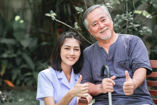 Hasta ile birlikte başparmak bankta oturan ile hemşire. Asyalı yaşlı adam ve birlikte konuşurken oturan bir genç bayan. Çok mutlu ruh hali.