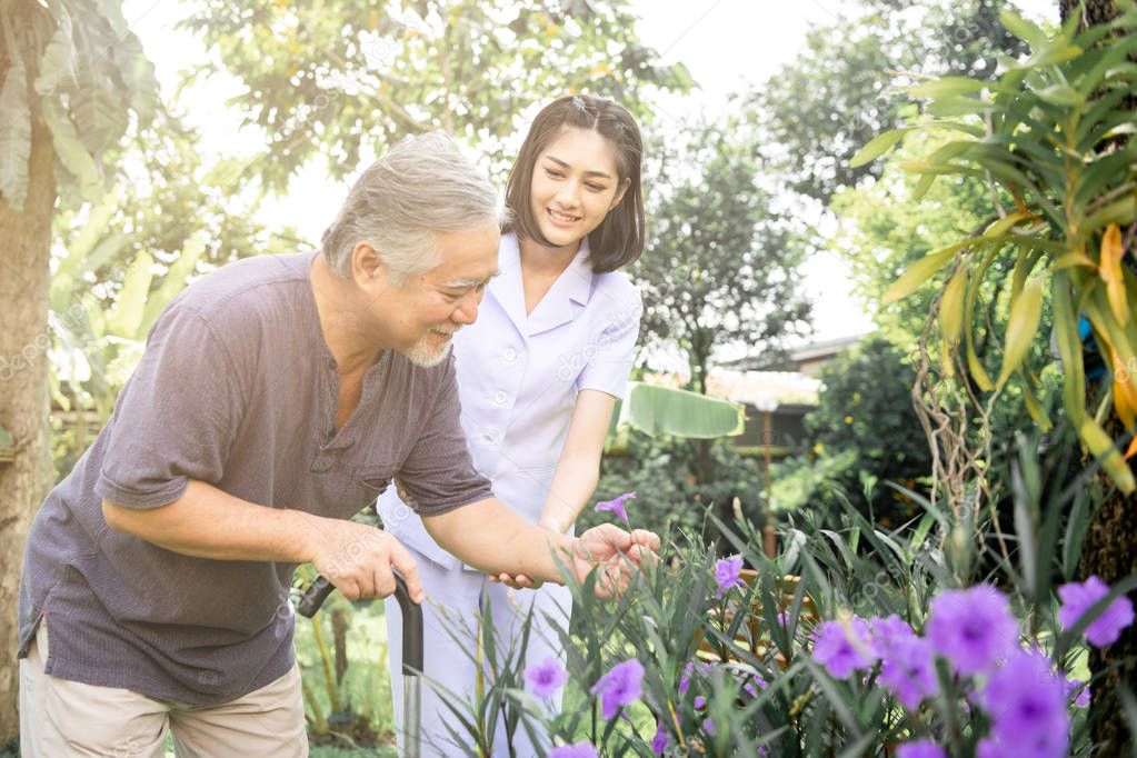 Comforting hand. Young nurse holding old man's shoulder in outdoor garden looking at flower. Senior care, care taker and senior retirement home service concept.