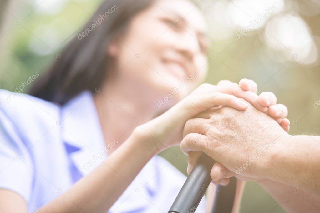 Comforting hand. Young nurse holding old man's hand in outdoor garden sitting on bench. Senior care, care taker and senior retirement home service concept.