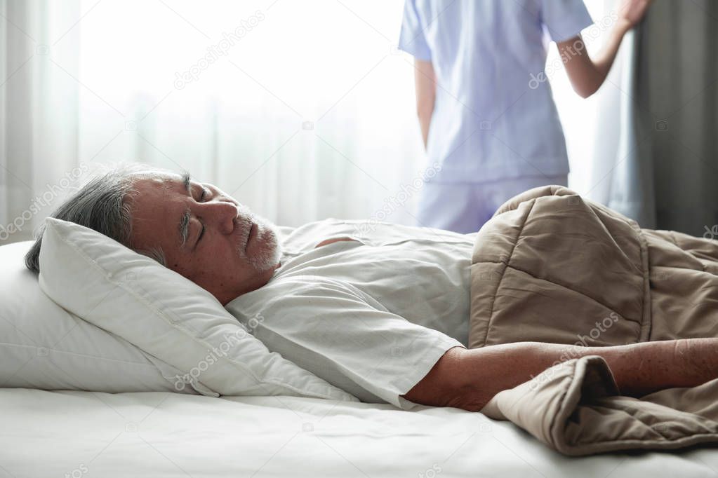 Senior man sleeping in bed and nurse open curtain. Old asian man and beautiful asian nurse woman in bedroom and open curtain. Senior home service concept. Close up shot.