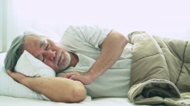 Beyaz arka plan üzerinde battaniyenin altında yatakta uyuyan gri saçlı Olgun Asyalı adam