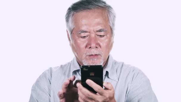 灰色の髪白い背景の上にスマート フォンを使用して驚かれる成熟したアジア男 — ストック動画