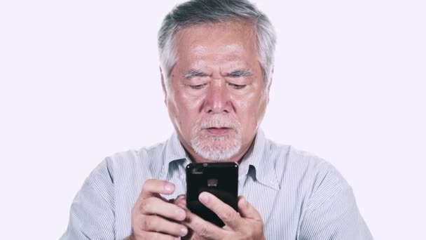 灰色の髪白い背景の上にスマート フォンを使用して怒っている成熟したアジアの男 — ストック動画