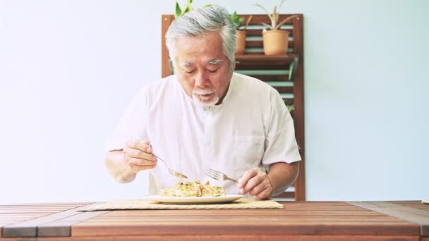 成熟的亚洲人在白色 T恤衫的灰色头发在现代内部吃食物 — 图库视频影像