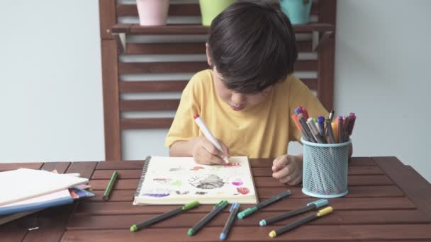 Азиатский Мальчик Рисует Картинки Маркером Блокноте Деревянном Столе — стоковое видео