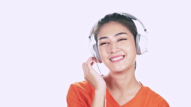 穿着白色耳机和橙色毛衣唱歌和听音乐在白色背景的愉快的亚洲妇女年轻人 — 图库视频影像