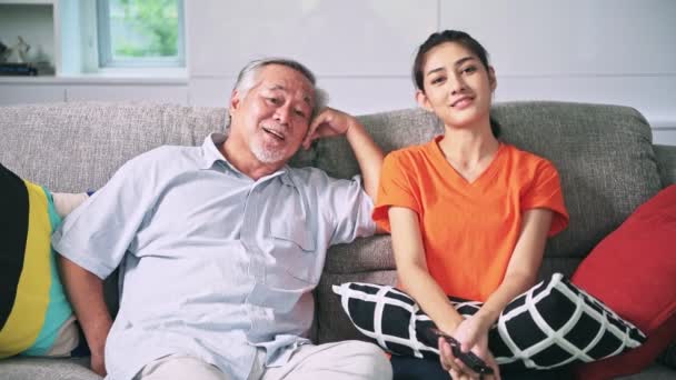 Asiatische Enkelin Mit Fernbedienung Und Großvater Sitzt Auf Der Couch — Stockvideo