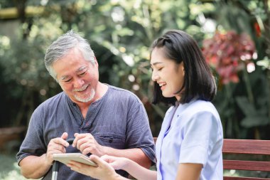 Hemşire hasta birlikte tablet vasıl seyir bankta oturmuş ile. Asyalı yaşlı adam ve birlikte konuşurken oturan bir genç bayan. Ruh sakin ol.