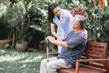 Hemşire ile hasta birlikte konuşurken bankta oturan. Asyalı yaşlı adam ve birlikte konuşurken oturan bir genç bayan. Ruh sakin ol.