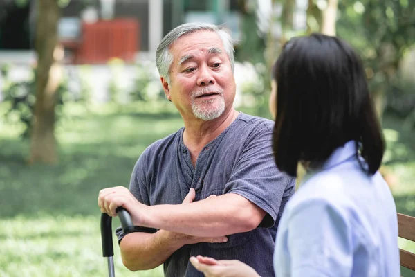 Hemşire ile hasta birlikte konuşurken bankta oturan. Asyalı yaşlı adam ve birlikte konuşurken oturan bir genç bayan. Mutlu bir gülümseme.