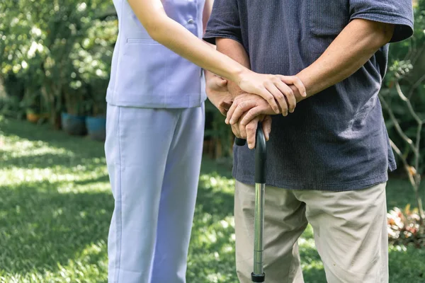 Comforting hand. Young nurse holding old man's hand in outdoor garden. Senior care, care taker and senior retirement home service concept. Close up shot.