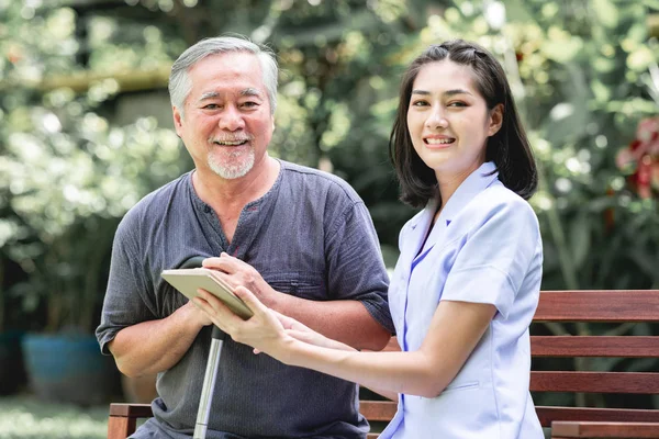 Νοσοκόμα Ασθενής Κάθεται Παγκάκι Μαζί Βλέπουν Tablet Ασιατικές Γέρος Και Εικόνα Αρχείου