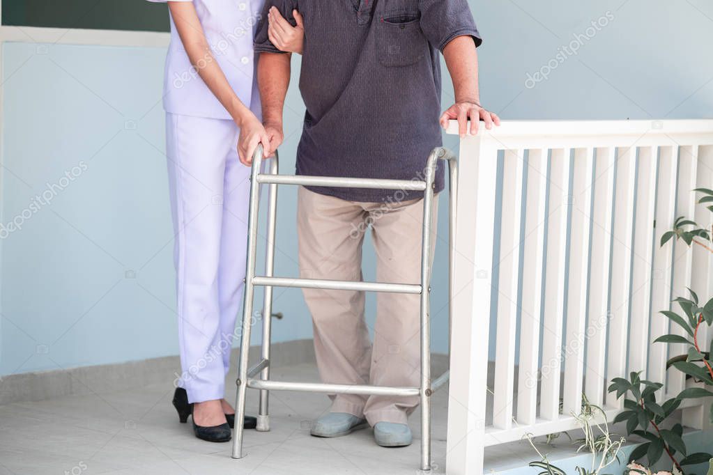 Nurse with patient using walker in retirement home. Young female nurse holding old man's hand in front of senior home. Senior care, care taker and senior retirement home service concept.