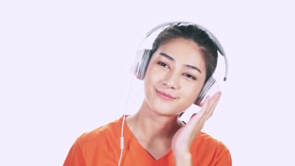 内容年轻的亚洲妇女穿着白色耳机和橙色毛衣听音乐在白色背景 — 图库视频影像
