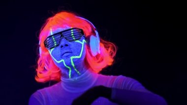 Dans ve kulaklık ile müzik dinlemek giyim gözlük, parlayan güzel seksi kadınla Uv cyborg yüz boyama, peruk. Asyalı kadın. Parti konsept.