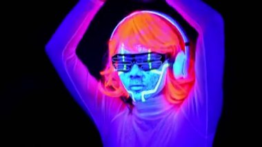 Dans ve kulaklık ile müzik dinlemek giyim gözlük, parlayan güzel seksi kadınla Uv cyborg yüz boyama, peruk. Asyalı kadın. Parti konsept.