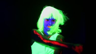 Güzel seksi kadın ile Uv yüz boyama, peruk, giyim kamera önünde dans parlayan ve kafa sallayarak atış omuz. Beyaz kadın. Parti konsept.