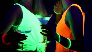 Güzel seksi kadın UV boya, parlak bilezik, İçecek, giyim birlikte kamera önünde, yakın kadar içki dans parlayan yüz. Beyaz ve Asyalı bir kadın. Parti konsept.