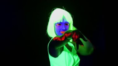 Güzel seksi kadın ile Uv yüz boyama, peruk, giyim kamera önünde dans parlayan, atış omuz. Beyaz kadın. Parti konsept.