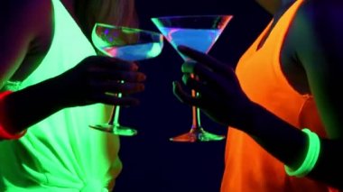 Güzel seksi kadın UV boya, parlak bilezik, İçecek, giyim birlikte kamera önünde, yakın kadar içki dans parlayan yüz. Beyaz ve Asyalı bir kadın. Parti konsept.