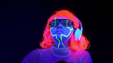 Dans ve kulaklık ile müzik dinlemek giyim gözlük, parlayan güzel seksi kadınla Uv cyborg yüz boyama, peruk. Asyalı kadın. Parti konsept.
