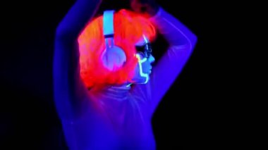 Dans ve kulaklık ile müzik dinlemek giyim gözlük, parlayan güzel seksi kadınla Uv cyborg yüz boyama, peruk. Asyalı kadın. Parti konsept.