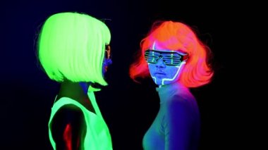 İle Uv yüz boyama, peruk, güzel seksi kadın giyim birlikte yavaş yavaş dans kamera önünde, yarım vücut vurdu parlayan gözlük, parlayan. Beyaz ve Asyalı bir kadın. Parti konsept.