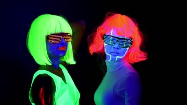 İle Uv yüz boyama, peruk, güzel seksi kadın giyim birlikte yavaş yavaş dans kamera önünde, yarım vücut vurdu parlayan gözlük, parlayan. Beyaz ve Asyalı bir kadın. Parti konsept.