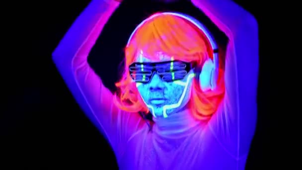 美しいセクシーな女性を紫外線サイボーグ顔ペンキ かつら 光る眼鏡 衣類ダンスとヘッドフォンで音楽を聴きます アジアの女性 パーティー コンセプト — ストック動画