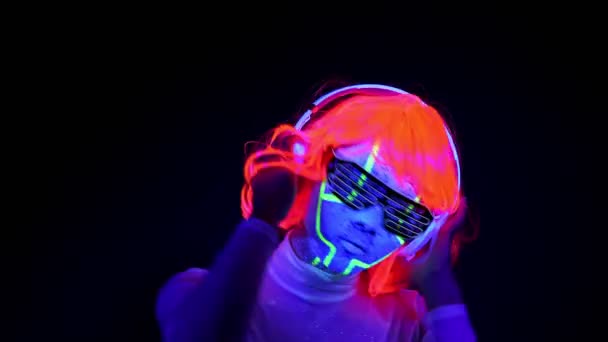美しいセクシーな女性を紫外線サイボーグ顔ペンキ かつら 光る眼鏡 衣類ダンスとヘッドフォンで音楽を聴きます アジアの女性 パーティー コンセプト — ストック動画