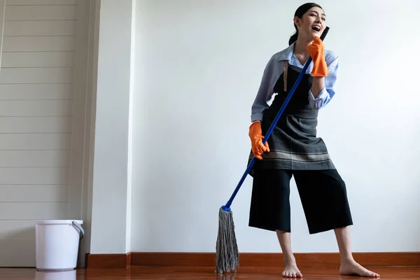 Woman cleaning house with mop stick. Beautiful Asian woman cleaning floor with mop stick, singing along the way. Low angle shot. House cleaning service concept.