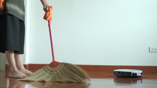妇女用扫帚棍打扫房子 美丽的亚洲妇女清洁地板与扫帚棒和清洁机器人 低角度拍摄 房屋清洁服务理念 — 图库视频影像