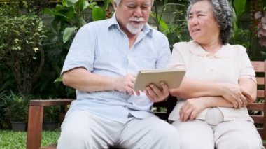 Oturma ve kullanarak üst düzey çift birlikte ev bahçesinde tablet. Emekli eski Asya erkek ve kadın, tablet, mutlu gülümseme haber okumak. Üst düzey yaşam tarzı kavramı. 