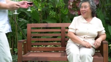 Oturan ve kırmızı şarap birlikte ev bahçesinde içme üst düzey bir çift. Emekli eski Asya erkek ve kadın, kocası karısına, mutlu gülümseme Şarap kadehi getir. Üst düzey yaşam tarzı kavramı. 