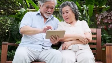 Oturma ve kullanarak üst düzey çift birlikte ev bahçesinde tablet. Emekli eski Asya erkek ve kadın, tablet, mutlu gülümseme haber okumak. Üst düzey yaşam tarzı kavramı. 