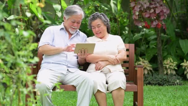 年配のカップルが座っているとを使用してタブレット一緒に家の庭で 引退した古いアジアの男性と女性 タブレット 幸せな笑顔でニュースを読みます シニアのライフ スタイルのコンセプト — ストック動画