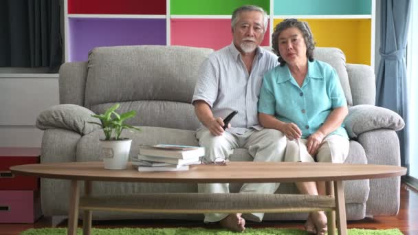 资深夫妇坐在客厅里看电视 退休的老亚洲男女 享受在客厅沙发上放松 快乐的微笑 老年人生活方式理念 — 图库视频影像