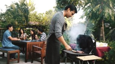 Barbekü Izgara açık ham burger hazırlama adam. Arka planda, arkadaşlarıyla birlikte konuşuyor. Ev partisi konsepti. 