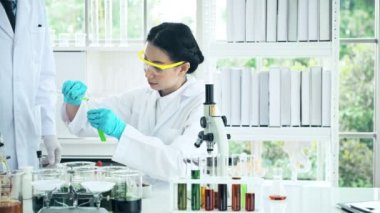 Asyalı kimyagerler laboratuarda çalışıyor. Kimyager test tüpüne kimyasal sıvı koyuyor. Bilim kavramı.