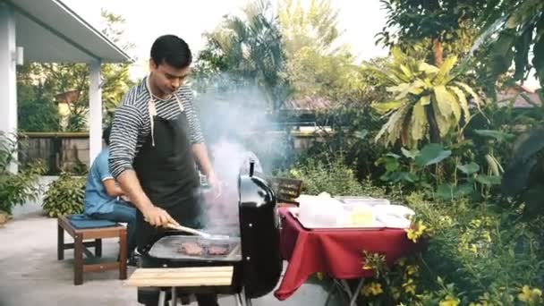 Człowiek Gotowanie Surowego Burger Grilla Grill Zewnątrz Przyjaciółmi Tle Śmiejąc — Wideo stockowe