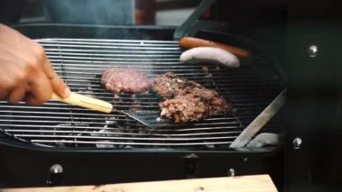 Küçük bir barbekü ızgara üzerinde çiğ pişmemiş burger ve sauages kapatın. Öğleden sonra beyaz bir adamla onu pişirmeye çalışırken..