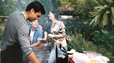 Adam barbekü ızgara açık çiğ burger pişirme. Arka planda arkadaşlarıyla birlikte gülüyor ve konuşuyorlar. House parti kavramı.