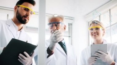 Bir laboratuarda çalışan kimyagerler grubudur. Genç erkek ve dişi kimyagerler cam ekran üzerinde yazma birlikte laboratuarda, çalışan üst düzey beyaz kimyager ile beyaz. Bilim kavramı.