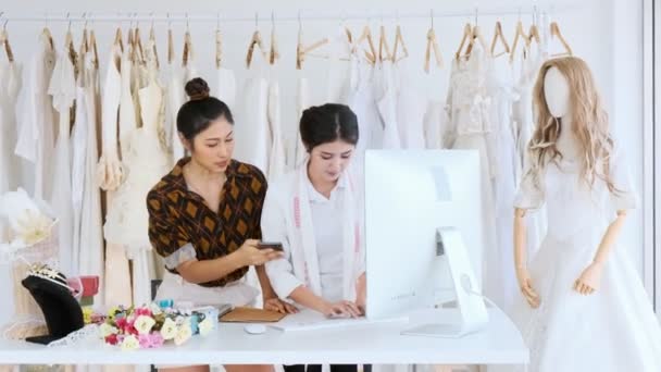 若者のファッション家のデザイナーが一緒に働きます ブライダル ドレス 顧客の注文を取って コンピューターとの若いアジアの女性 スモール ビジネス コンセプト — ストック動画